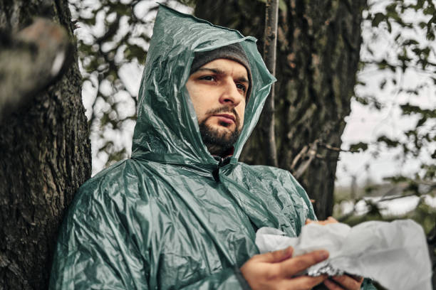 a man with a beard in a green raincoat eats in nature. cloudy weather, fast food. - 11305 imagens e fotografias de stock