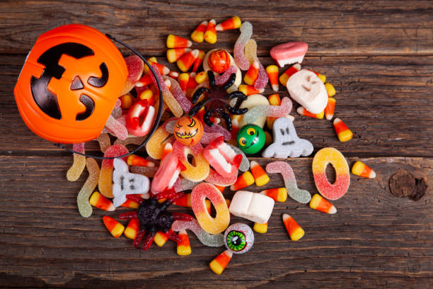 halloween jack o lantern pail with bottom border of spilling candy over brown wood - dark candy imagens e fotografias de stock