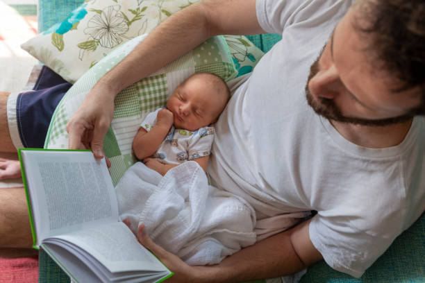 Father reading paper book with baby on lap stock photo