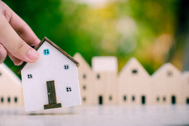 istock Hand choosing mini wood house model from model on wood table, selective focus, Planning to buy property. Choose what's the best. A symbol for construction ,ecology, loan concepts 1278509621