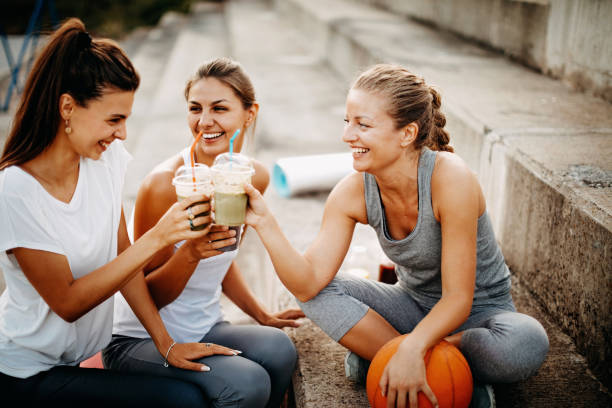 Cheers, get ready for training Women preparing for training outdoor, drinking smooothie asphalt basketball court stock pictures, royalty-free photos & images