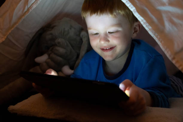 istock Young Boy Using tech or watching a film on digital tablet in the darkness of a camp 1278515182