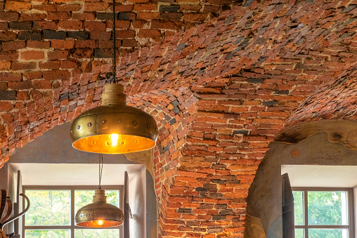 Retro style copper, brass or bronze luminaire on red brick vaulted ceiling. Horizontal orientation, selective focus.