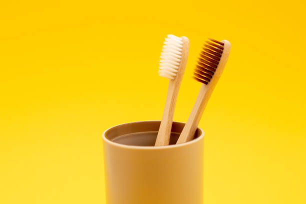 istock Two bamboo toothbrushes in glass on yellow background 1278528213