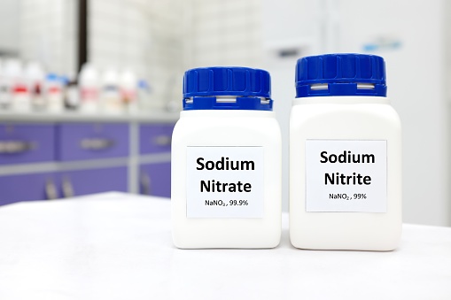 Selective focus of bottles of pure sodium nitrite and sodium nitrate chemical compound preservative or food additive. White laboratory background with copy space.