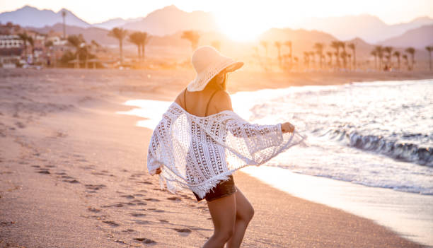 Woman at sunset on the beach in a hat. A beautiful boho model in a white Cape and swimsuit poses on the beach in the sunlight Crochet stock pictures, royalty-free photos & images