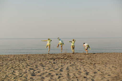 Wide shot of Montegrin beach in Ulcinj where four excited friends jump and enjoy the summer vacations. Their bodies are full of colorful powder after a party.
