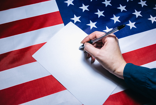 American flag with dollars on it. Elections in the USA. Woman putting tick on the paper for vote. Political changes in the country. Copy space place.