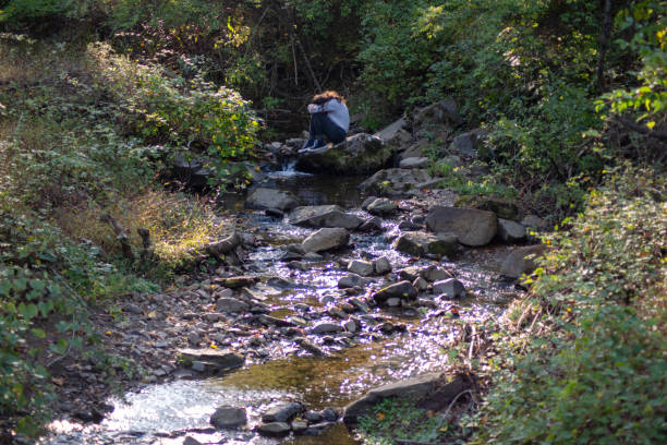 istock Sad young man sits alone by a forest stream covering his face 1278548429