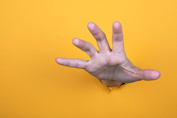 istock Hand reaches for help. Yellow paper background. Copy space 1278549991