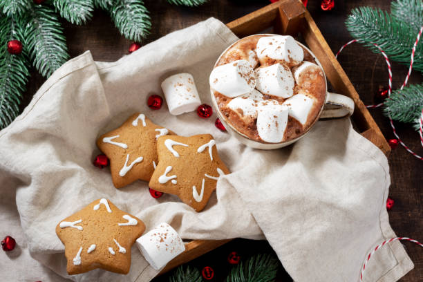 istock Hot cocoa or hot chocolate in a ceramic Cup on a wooden tray surrounded by gingerbread, Christmas tree branches and ornaments on a brown wooden table. Christmas Flatley 1278550146