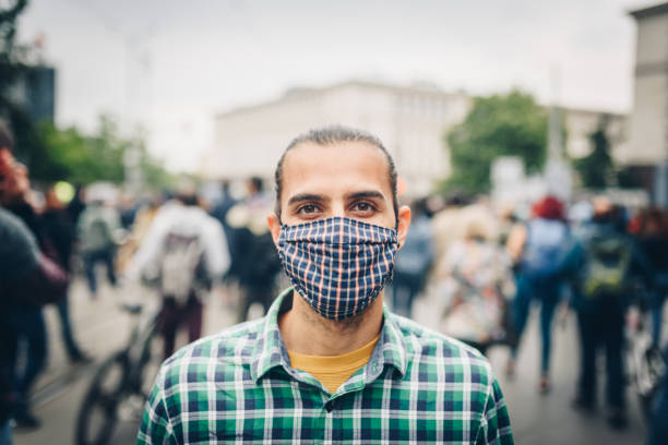 giovane con una maschera circondata da una folla in città. inquinamento atmosferico / protezione dal coronavirus / concetto di protesta. - clothing protective workwear authority anticipation foto e immagini stock