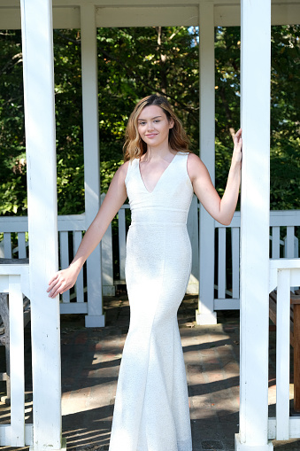Teenage girl outdoors wearing a prom dress which is off white and silver