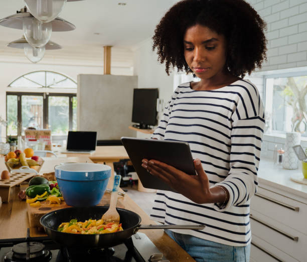 istock Concentrated mixed race female reading recipe off digital tablet while making dinner in modern kitchen 1278555632