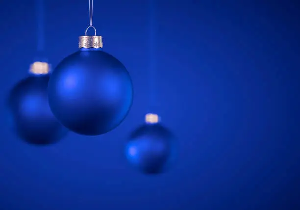 Three blue Christmas balls. Solid matt Christmas ornaments hanging against royal blue background. Christmas decoration, festive atmosphere concept. Selective focus, copy space.