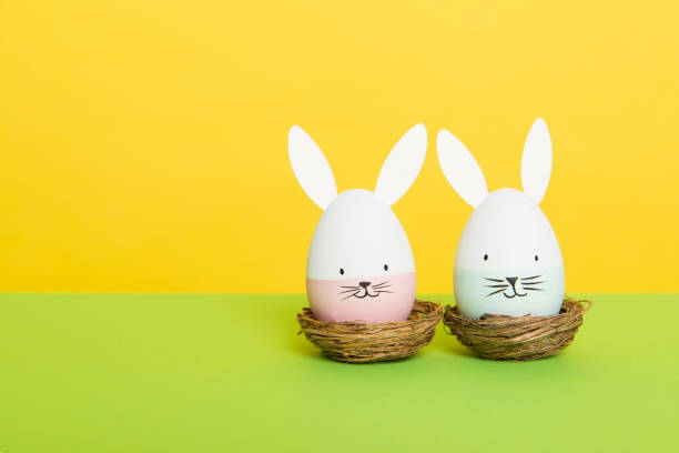 istock Two easter eggs with bunny faces in nest on a green and yellow background with space for copy 1278560077