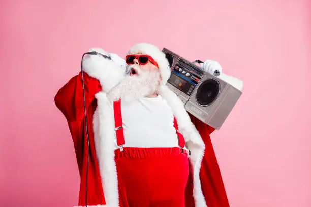 Cool north-pole pop star celebrity white grey hair beard santa claus big abdomen sing x-mas, christmas songs hold mic boom box wear suspenders sunglass cap isolated pastel color background