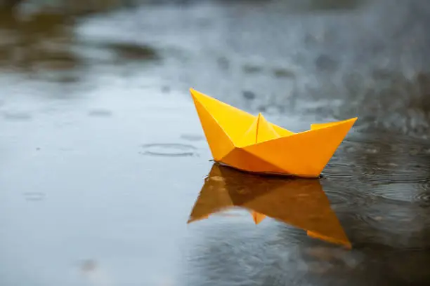 Paper handmade yellow boat toy on a puddle in a rain