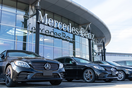 Mercedes-Benz text logo hanging at the front of a Burlington Ontario dealership with new cars parked in-front.
