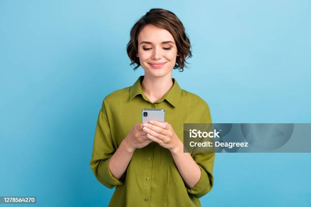 Photo Of Lovely Cute Lady Short Hairdo Hands Hold Telephone Look Screen Smile Read Typing Write Wear Green Shirt Isolated Blue Color Background Stock Photo - Download Image Now