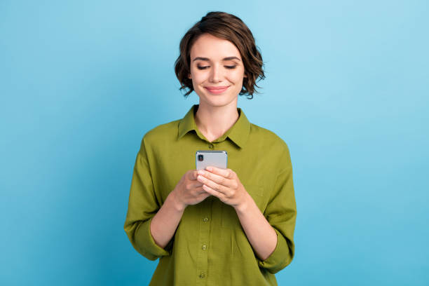 photo of lovely cute lady short hairdo hands hold telephone look screen smile read typing write wear green shirt isolated blue color background - woman phone imagens e fotografias de stock
