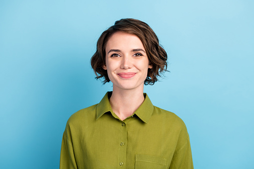 Photo portrait of cute smiling pretty girl with brunette short hair wearing green shirt, isolated on blue color background