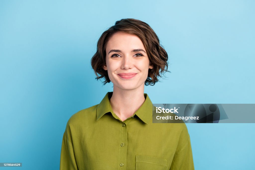 Photo portrait of cute smiling pretty girl with brunette short hair wearing green shirt isolated on blue color background Photo portrait of cute smiling pretty girl with brunette short hair wearing green shirt, isolated on blue color background Portrait Stock Photo