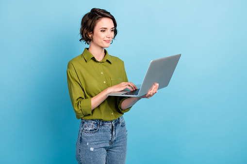 Photo of charming lady short hairstyle hold netbook, hand touchpad wear jeans green shirt isolated blue color background