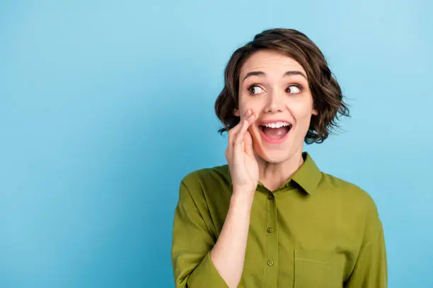 Photo of Photo portrait of young pretty girl with short hair telling secret information rumouring gossiping wearing green shirt isolated on blue color background