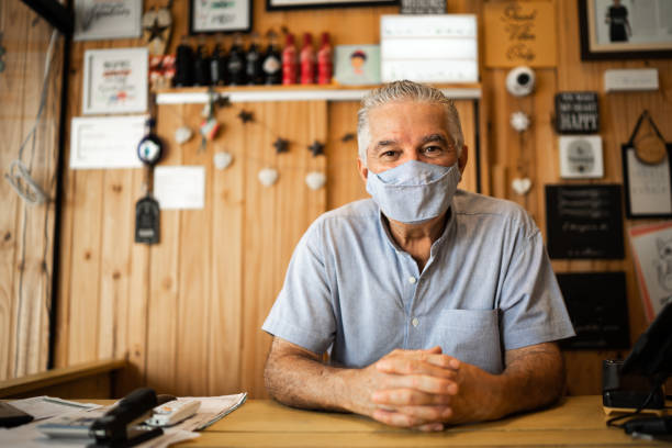 porträt eines älteren mannes mit gesichtsmaske, die in einem geschäft arbeitet - markt verkaufsstätte fotos stock-fotos und bilder