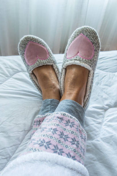 старшая женщина ноги на кровати просыпаться в уютных тапочках - slipper senior adult shoe human leg стоковые фото и изображения