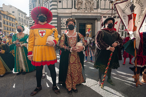 Florence, Italy - 2020, September 26:
Figurants wearing Florentine Republic costumes, during the historical reenactment ”Bacco Artigiano 2020 Festival”. They carry gift of traditional Chianti wine flasks.
Baptistery of San Giovanni in the background.