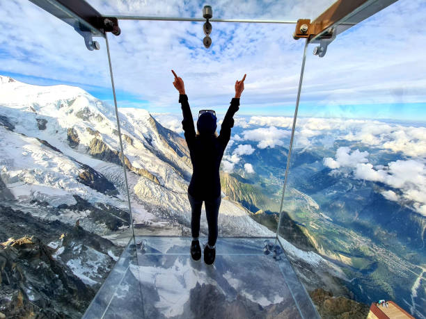 frau bewundert den blick aus dem glaskasten, der schritt in die leere - aiguille du midi skywalk - erhöhter fußgängerweg stock-fotos und bilder