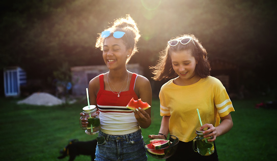 Cheerful young teenager girls friends outdoors in garden, carrying watermelon.
