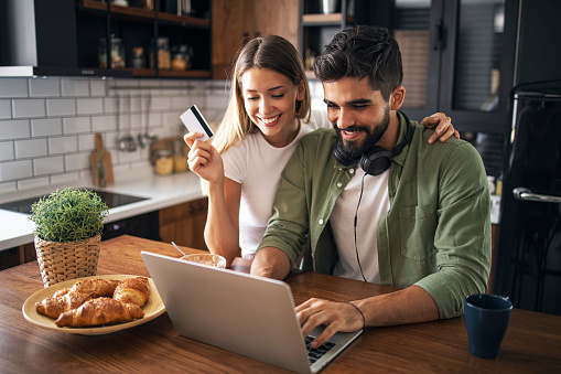 Pretty lady is holding credit card for online shopping with her boyfriend. Happy couple looking at laptop