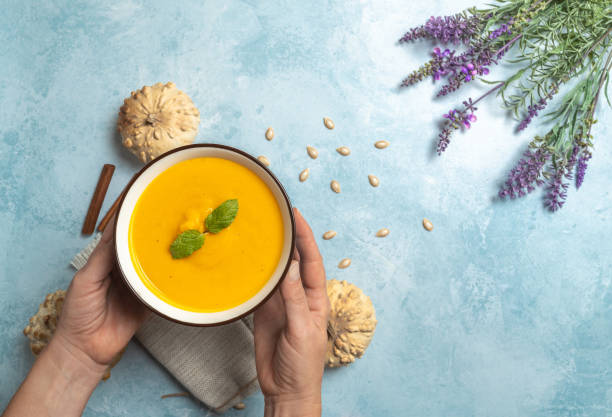 istock Hands holding bowl of pumpkin cream on blue rustic background 1278590004