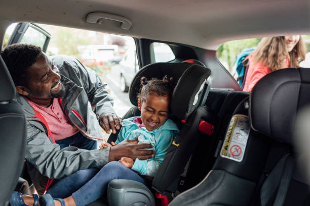 Safety can be Fun! Father buckling his young daughter into a car seat while tickling her. They are going on a road trip together. Taken during the Covid 19 pandemic. northern europe family car stock pictures, royalty-free photos & images