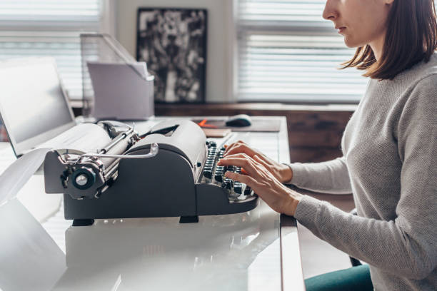 scrittrice che digita su una macchina da scrivere seduta nella sua stanza di lavoro. - machine typewriter human hand typing foto e immagini stock