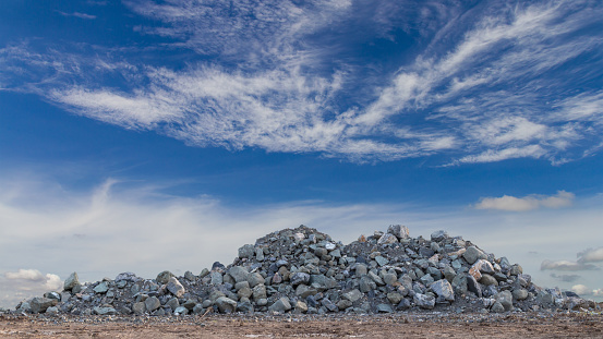 A large granite pile like a mountain on the ground with a cloud of skies is a backdrop during the day.