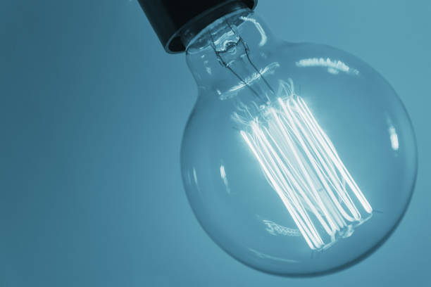 istock Vintage light bulb on blue background, closeup. Glowing edison bulb 1278593749