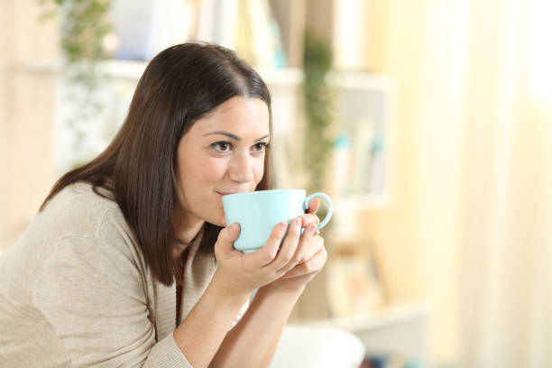 istock Happy woman drinking coffee sitting on a sofa at home 1278595206