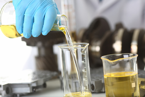 Close up of male hands in blue sterile gloves pouring yellow liquid into glass tube in laboratory