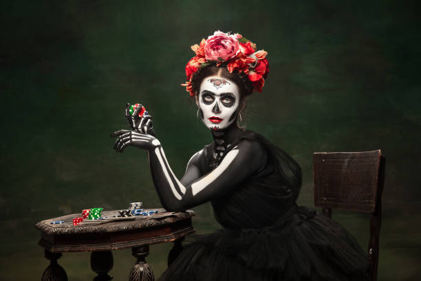 Young girl in the image of Santa Muerte, Saint death or Sugar skull with bright make-up. Portrait isolated on studio background. Gambling. Young girl like Santa Muerte Saint death or Sugar skull with bright make-up. Portrait isolated on dark green studio background with copyspace. Celebrating Halloween or Day of the dead. muerte stock pictures, royalty-free photos & images