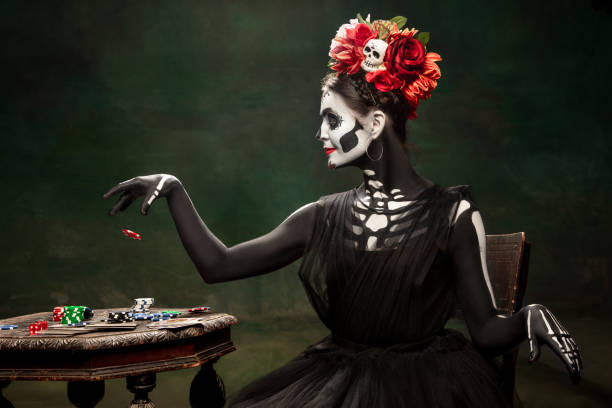 Young girl in the image of Santa Muerte, Saint death or Sugar skull with bright make-up. Portrait isolated on studio background. Casino. Young girl like Santa Muerte Saint death or Sugar skull with bright make-up. Portrait isolated on dark green studio background with copyspace. Celebrating Halloween or Day of the dead. muerte stock pictures, royalty-free photos & images