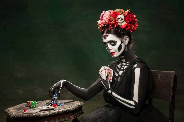 Young girl in the image of Santa Muerte, Saint death or Sugar skull with bright make-up. Portrait isolated on studio background. Gambling. Young girl like Santa Muerte Saint death or Sugar skull with bright make-up. Portrait isolated on dark green studio background with copyspace. Celebrating Halloween or Day of the dead. muerte stock pictures, royalty-free photos & images