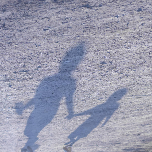 Close-up image of the shadow of two people walking on the ground near rural road to sunlight.
