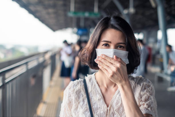 Asian woman wearing face mask for prevent dust pm 2.5 bad air pollution and coronavirus or covid19 having a dry cough. Girl avoiding smell and protect virus infection from people at train station. mujer asiática que usa mascarilla facial para prevenir el polvo pm 2.5 mala contaminación del aire y coronavirus o covid19 tener una tos seca. niña evitando el olor y proteger la infección por virus de las personas en la estación de tren.