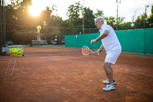 Active senior man playing tennis on tennis court
