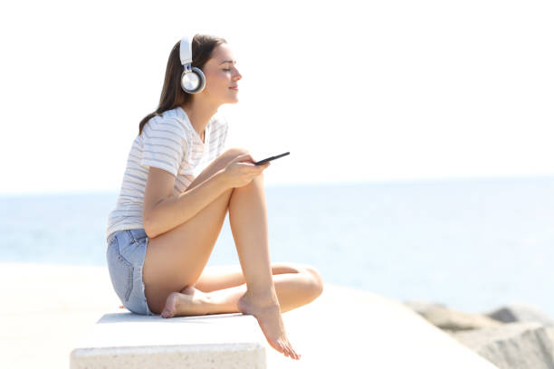 расслабленная женщина с длинными ногами слушает музыку на пляже - leg waxing audio стоковые фото и изображения