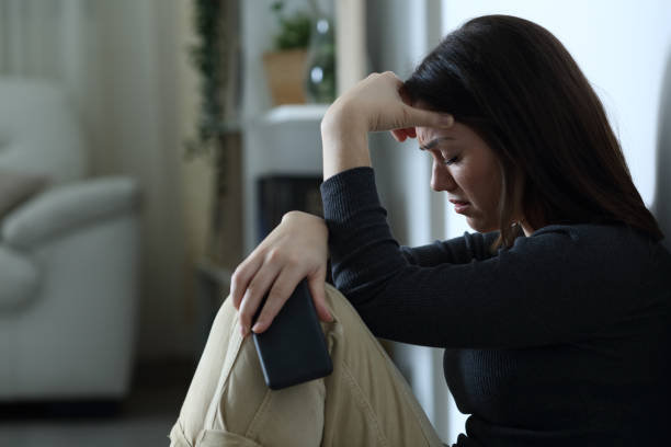 sad woman holding smart phone complaining at home - waiting telephone on the phone anxiety imagens e fotografias de stock